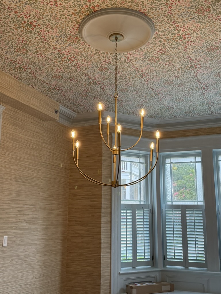 Botanical ceiling wallpaper and brass chandelier over natural grasscloth walls