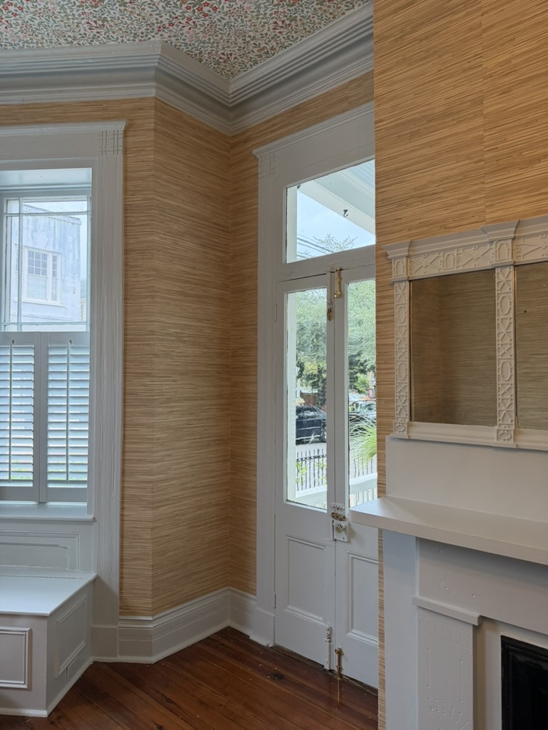 Grasscloth walls surrounding a white historic fireplace mantel and tall glazed door