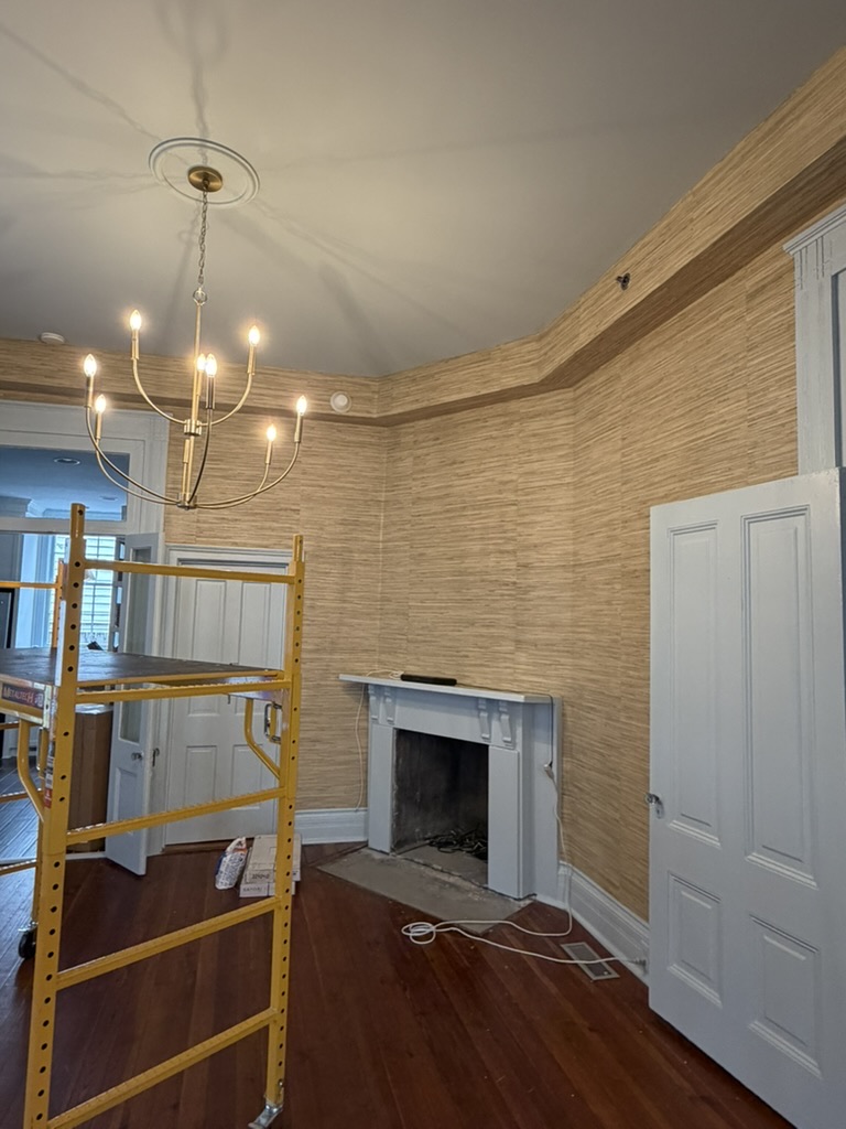Natural grasscloth wallcovering installation in progress around a fireplace and historic woodwork
