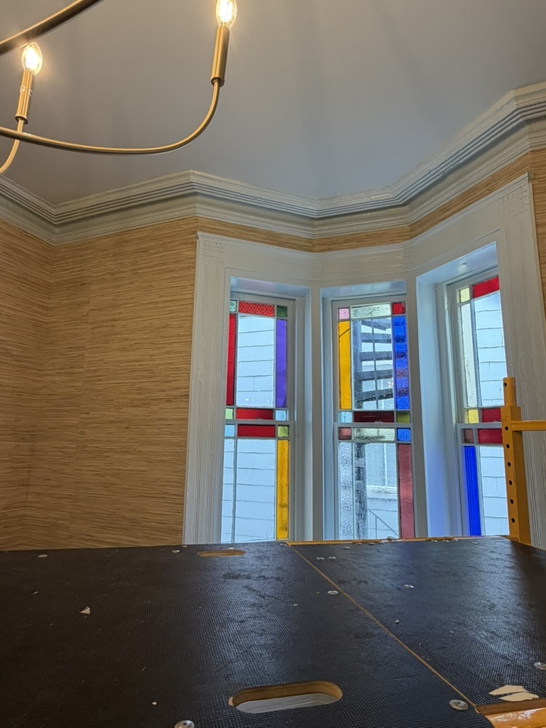 Grasscloth installation beside colorful historic stained-glass bay windows in the Tri Delta house