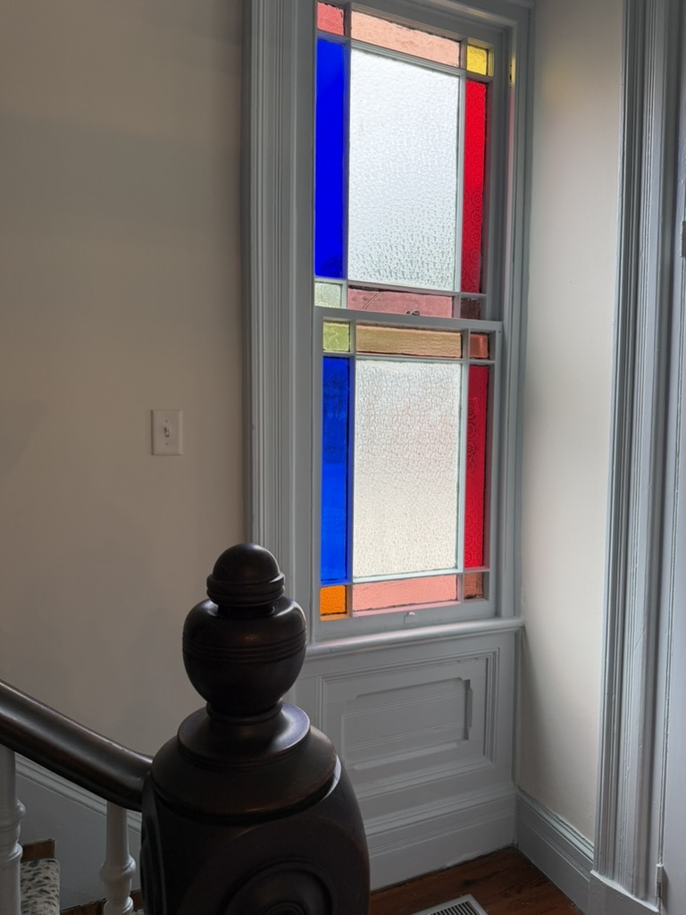 Red blue amber and textured stained-glass sash window above a historic stair landing