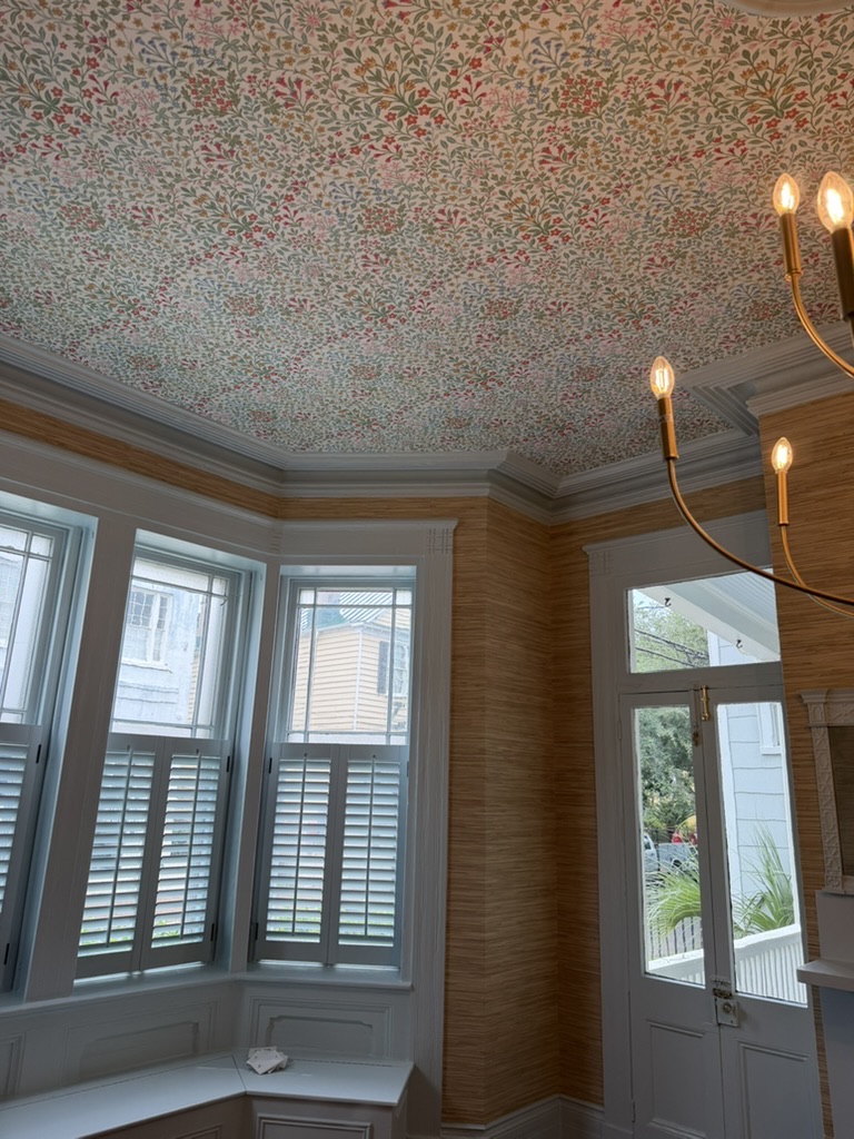 Floral wallpapered ceiling above grasscloth walls and a historic Charleston bay window